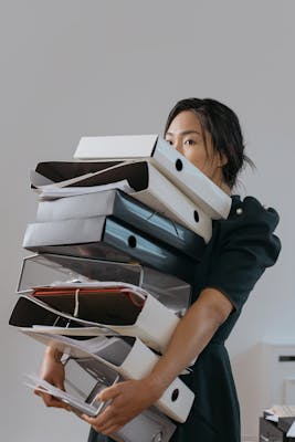Young woman with dark hair carrying an armful of plastic binders.